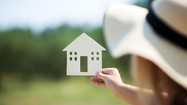 A woman holding up a house cut out. There is a field of green in the background.