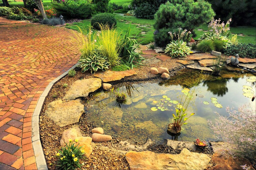 Natural pool surrounded by rocks, a lush green landscape, and a clay paver walkway.